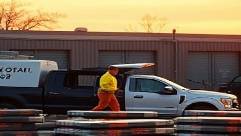 systematic biohazard removal, unwavering, loading debris, photorealistic, near a temporary storage site with nearby vehicles, highly detailed, dust particles visible in air, high definition, warm orange and brown tones, evening light, shot with a 60mm lens.
